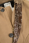 Close-up of a tan jacket with a zipper and decorative band, featuring a brand label.