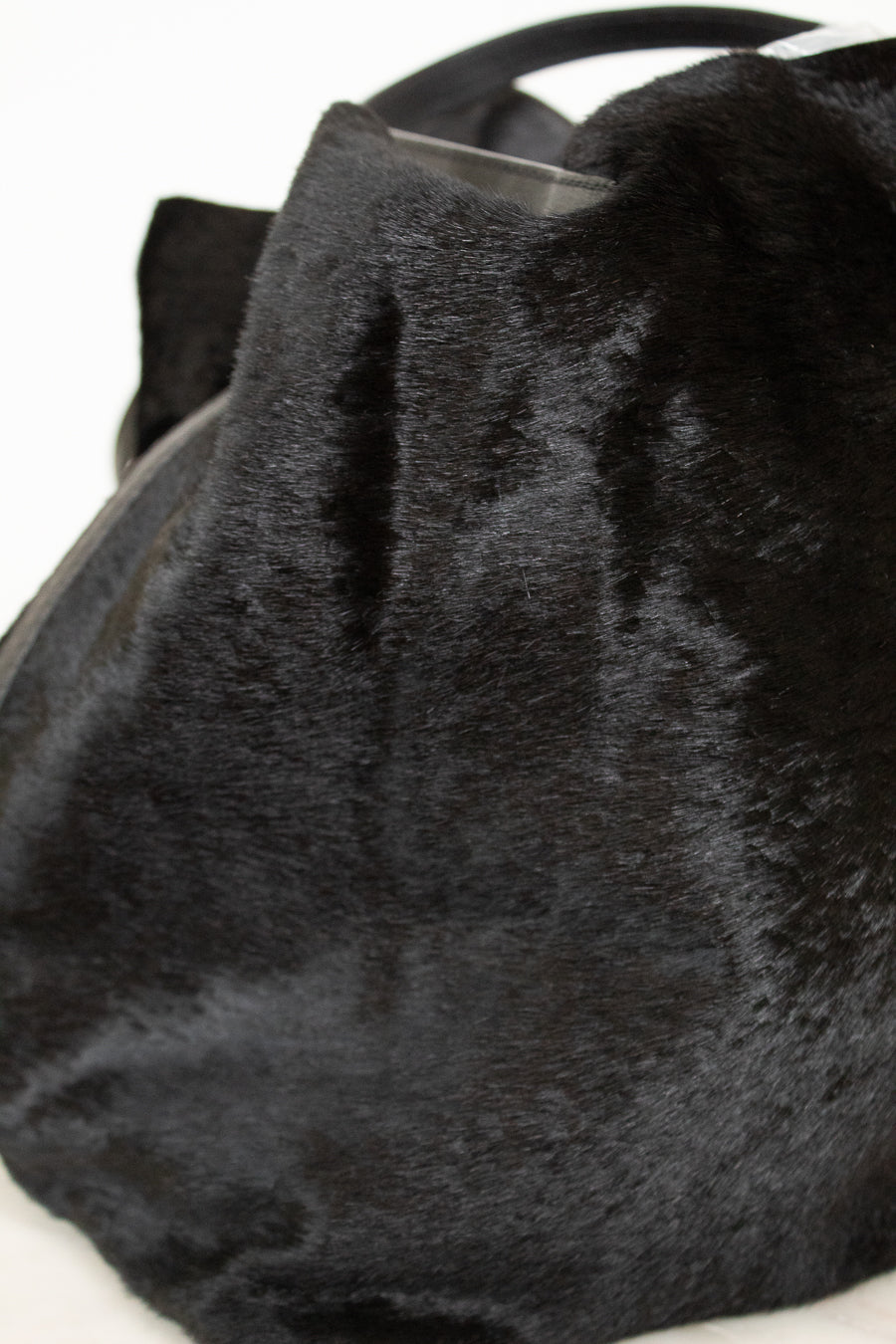 Close-up of a black faux fur handbag or purse showing the soft textured material and a dark handle against a plain white background.