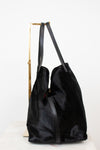 A black faux fur  tote bag with black leather shoulder straps, displayed on a gold metal stand against a white background.