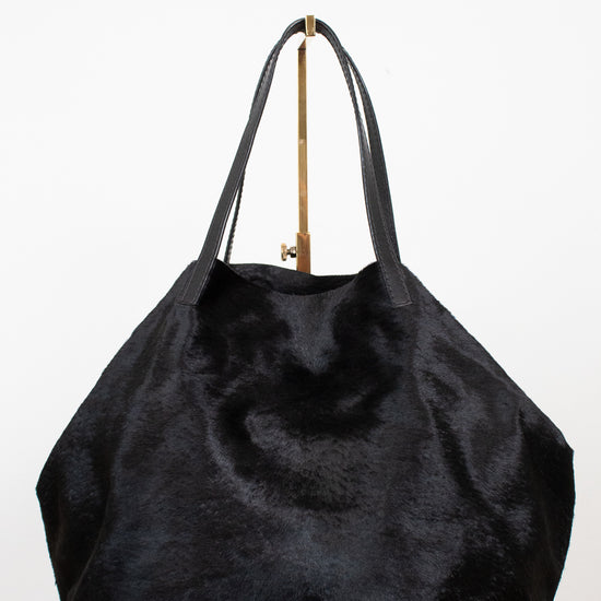 A large black faux fur tote bag with black leather shoulder straps, displayed on a white surface against a white background.