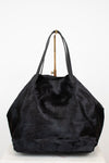 A large black faux fur tote bag with black leather shoulder straps, displayed on a white surface against a white background.