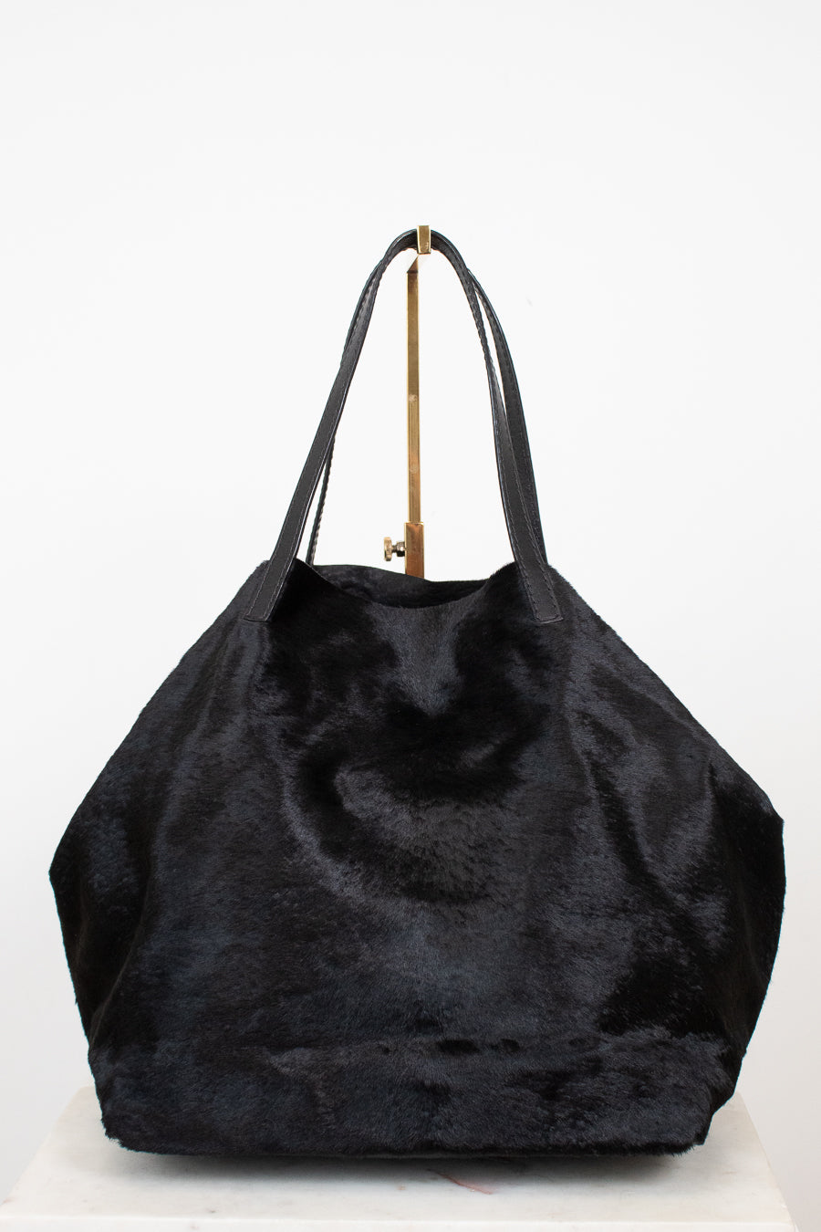 A large black faux fur tote bag with black leather shoulder straps, displayed on a white surface against a white background.