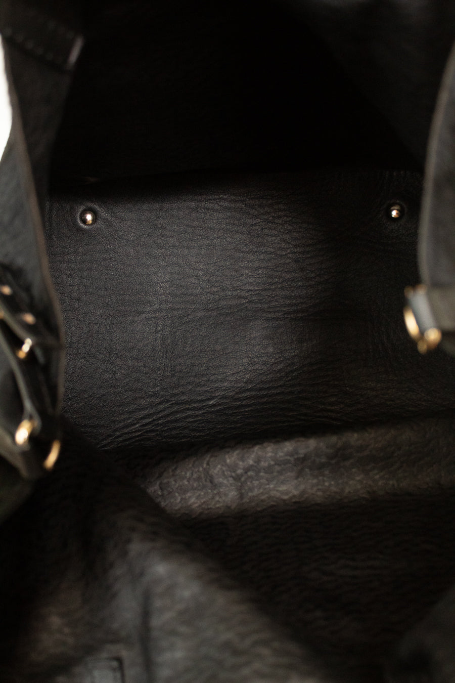 Close-up of the interior of a black textured leather bag, showing the black leather lining, metal rivets, and a sliver of the black exterior material with gold-tone hardware on the sides.