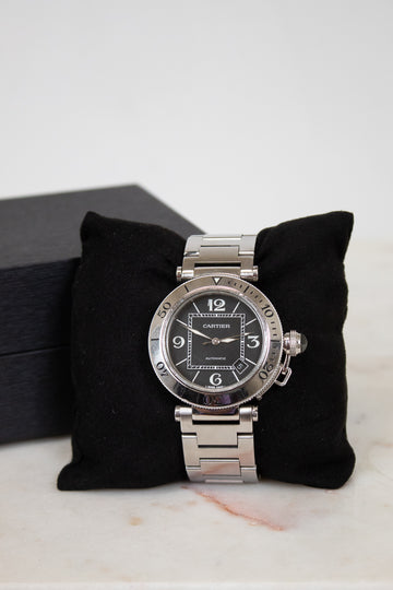 Silver Cartier watch on a black cushion with a white background