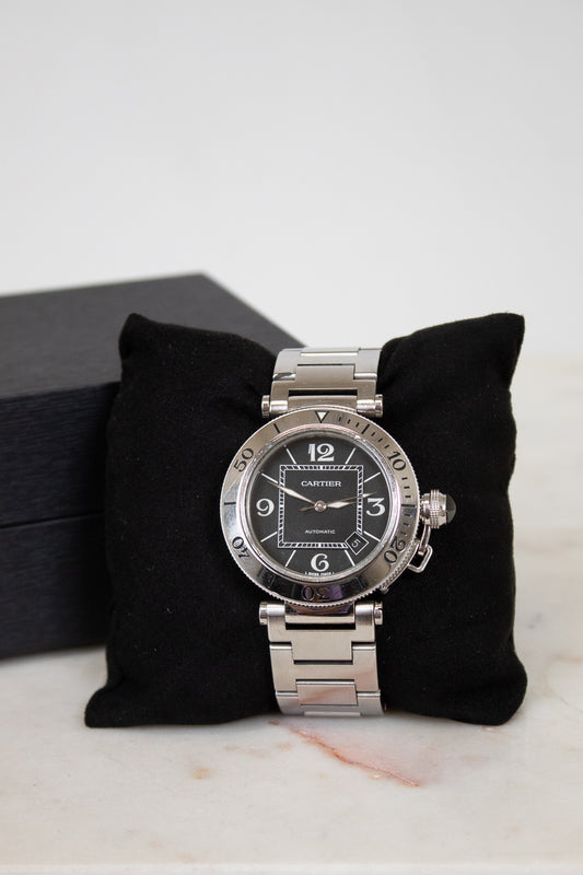 Silver Cartier watch on a black cushion with a white background