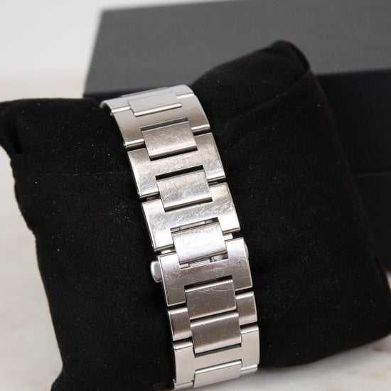 Silver watch band on a black cushion with a white background