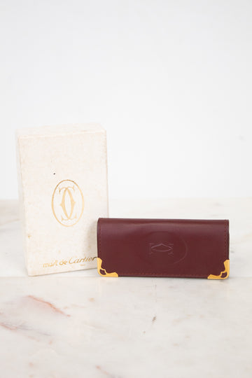 Burgundy leather key holder with gold accents on a marble surface, next to a white card with a logo.