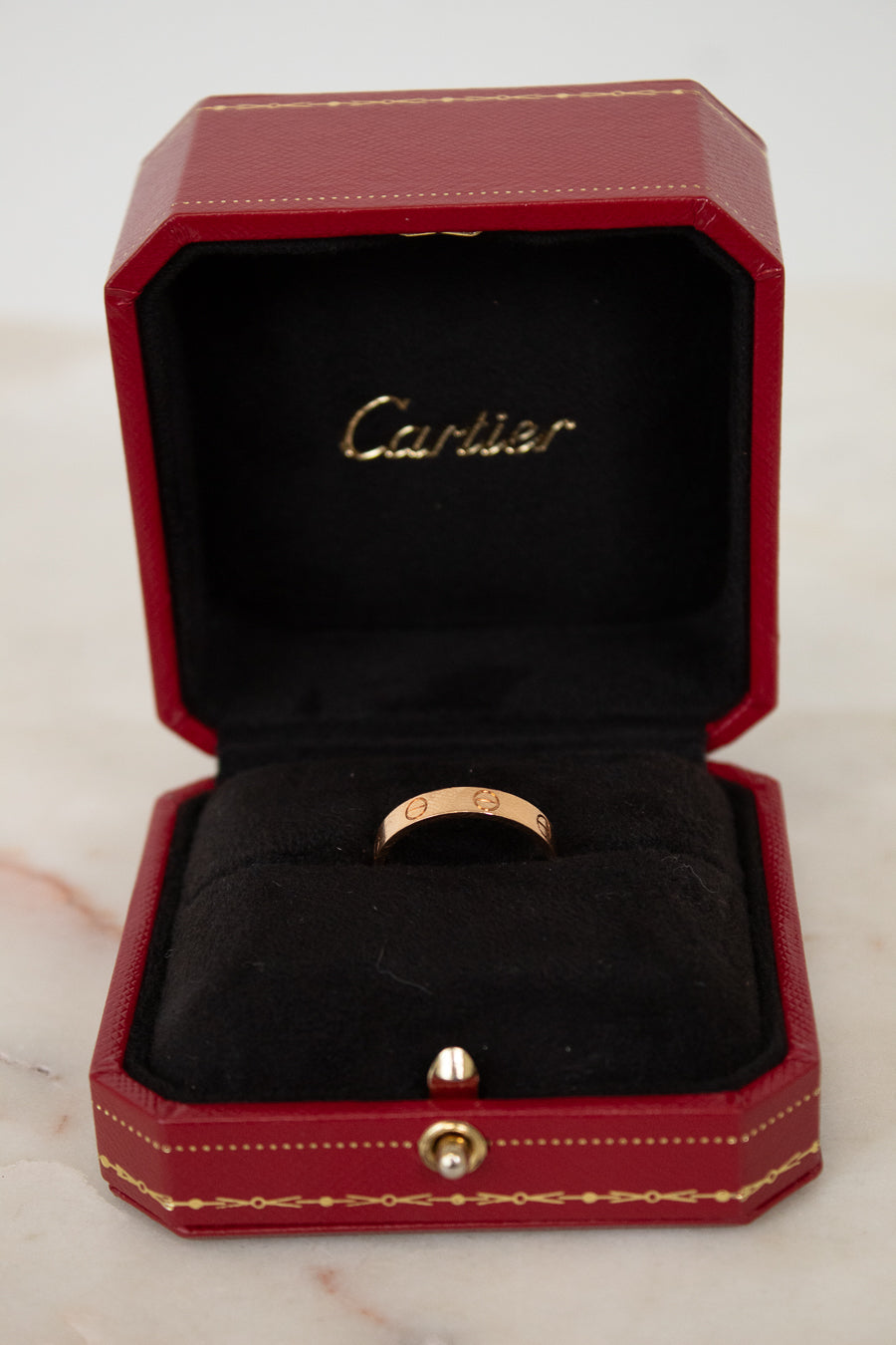 Rose gold ring in a red Cartier box on a marble surface