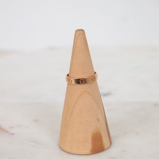 Wooden cone-shaped ring holder with a rose gold ring on a light background