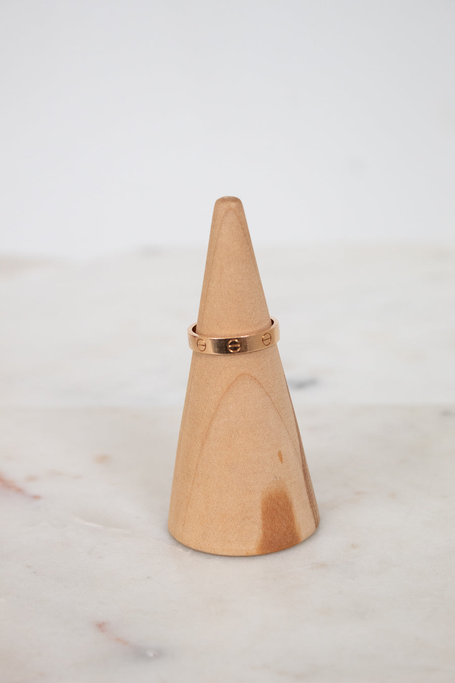 Wooden cone-shaped ring holder with a rose gold ring on a light background