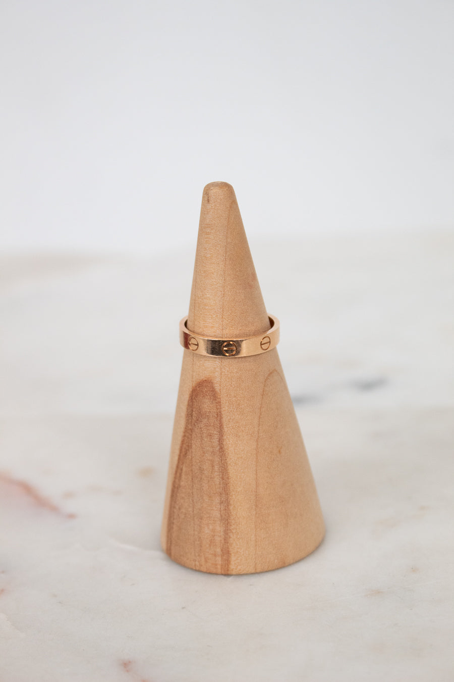 Wooden cone with a rose gold ring on a marble surface