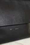 Close-up of a black leather clutch bag with 'Celine' branding on a marble surface.