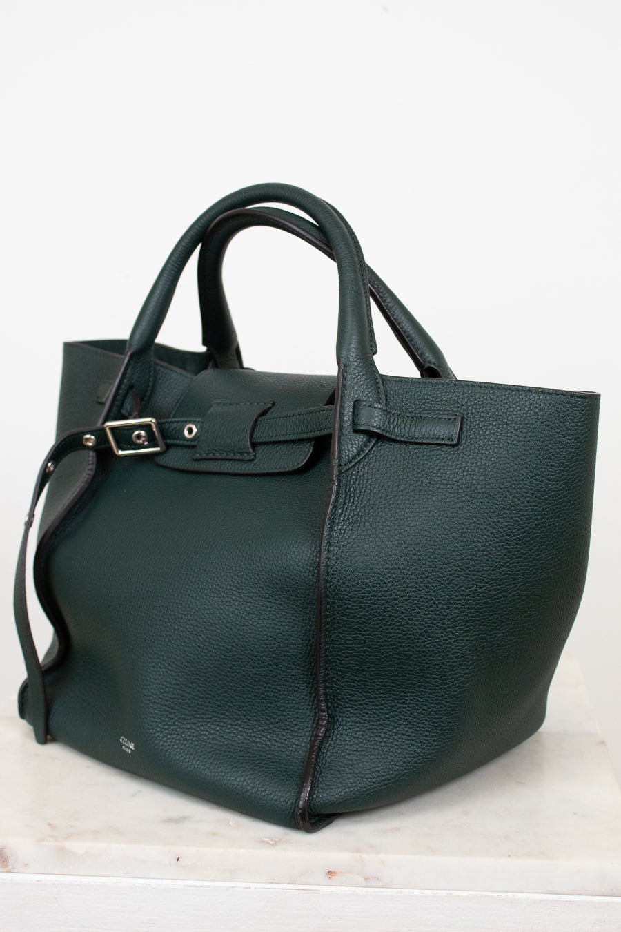 Green leather handbag on a light marble surface with a white background