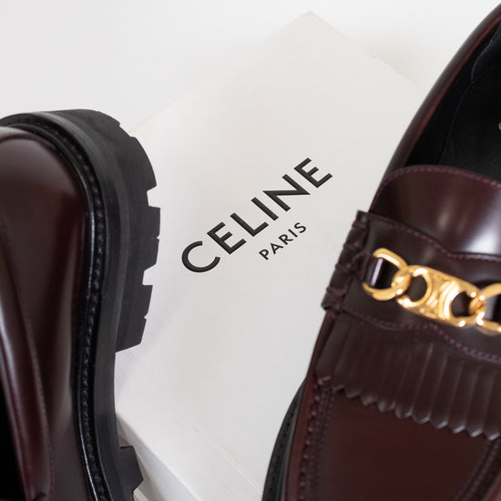 Brown loafers with gold chain detail on a Celine box