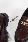 Brown loafers with gold chain detail on a Celine box
