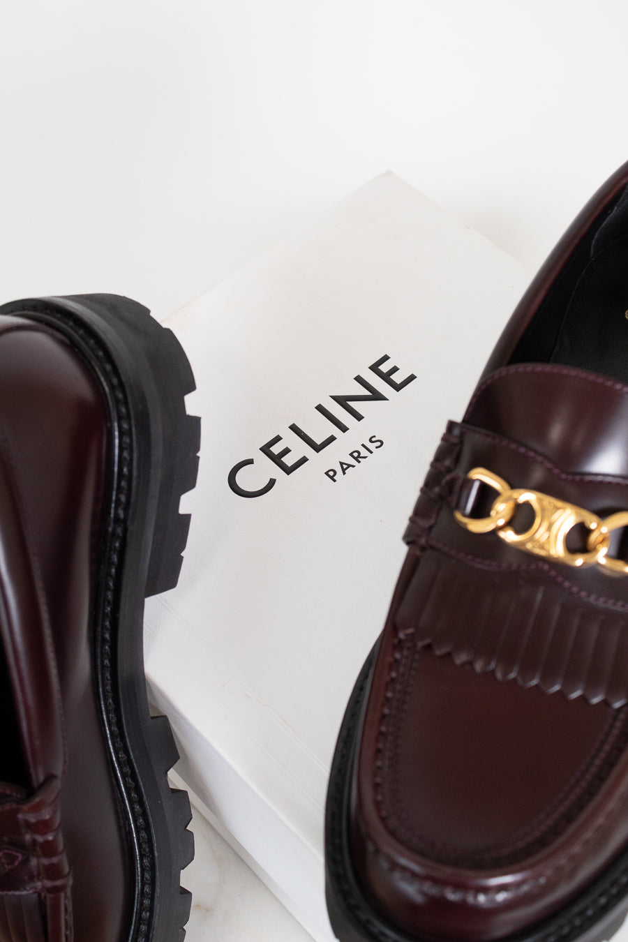 Brown loafers with gold chain detail on a Celine box