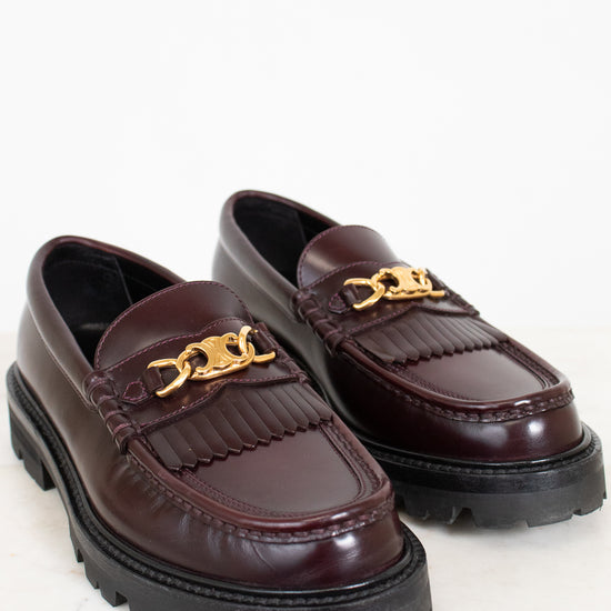Pair of brown loafers with gold chain details on a white background