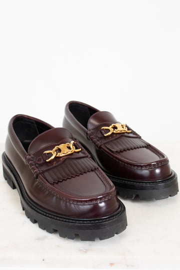 Pair of brown loafers with gold chain details on a white background