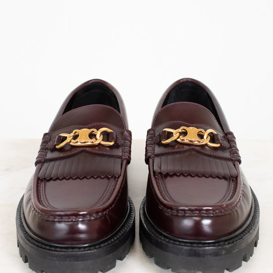 Pair of brown loafers with gold chain detail on a white background