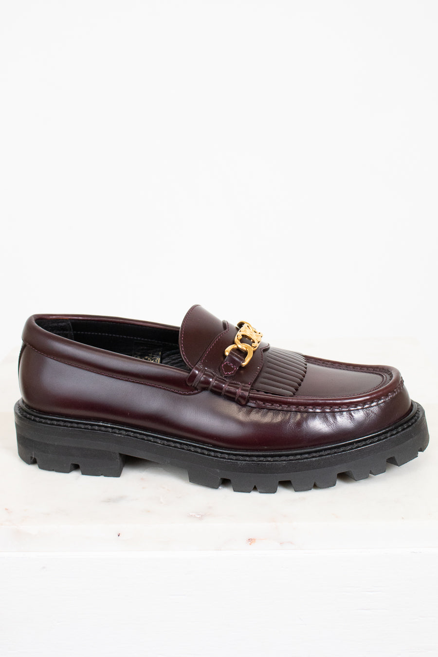 Brown loafer shoe with gold buckle on a white background