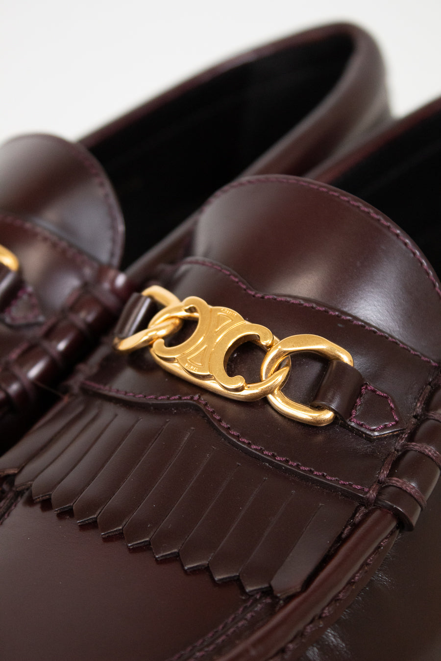 Brown loafers with gold chain detail on a white background