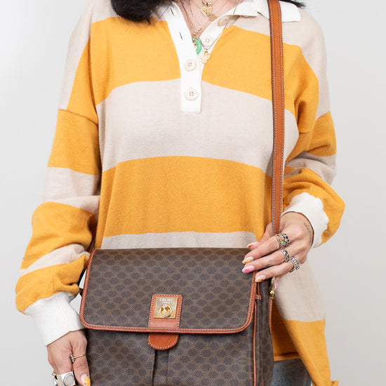 Person wearing a striped shirt holding a brown patterned bag against a plain background
