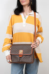 Person wearing a striped shirt holding a brown patterned bag against a plain background