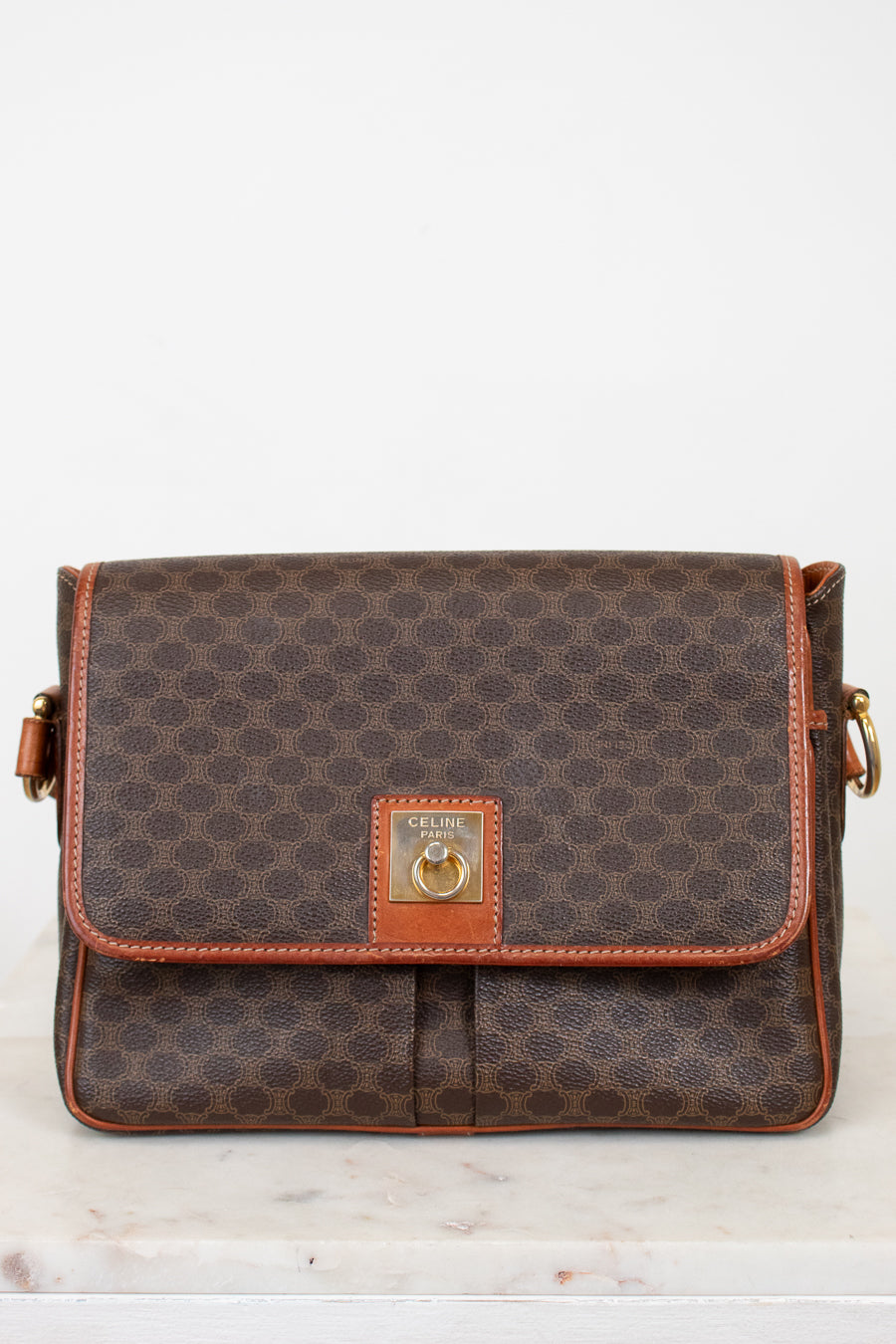 Brown patterned handbag with gold accents on a white background