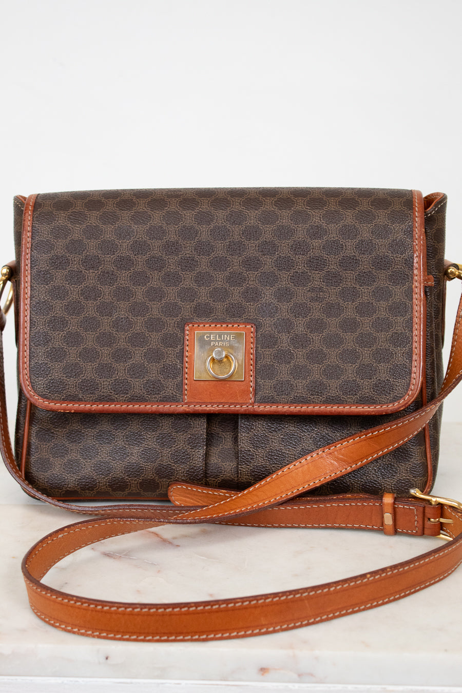 Brown patterned handbag with tan leather strap and accents on a white background