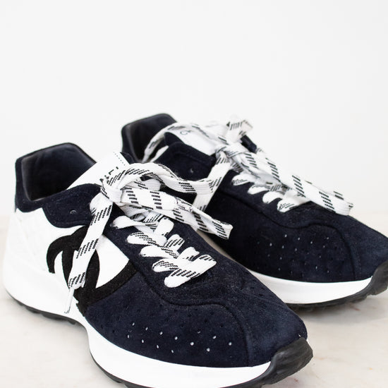 Pair of Chanel navy blue sneakers with white laces on a light gray background