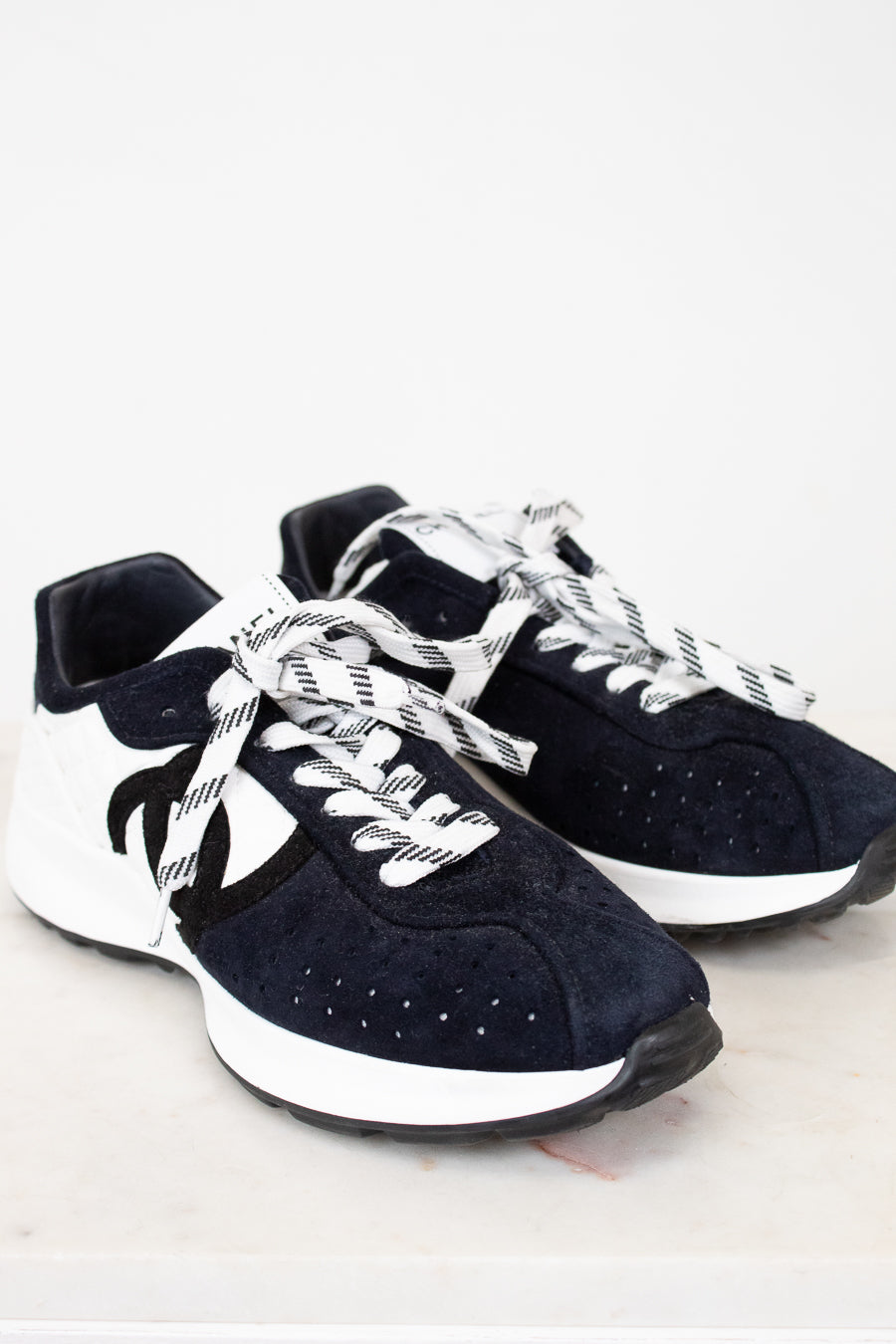 Pair of Chanel navy blue sneakers with white laces on a light gray background