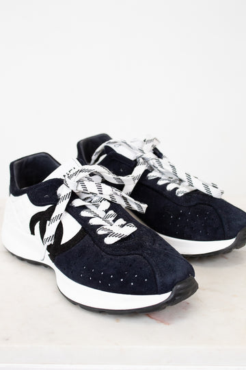 Pair of Chanel navy blue sneakers with white laces on a light gray background