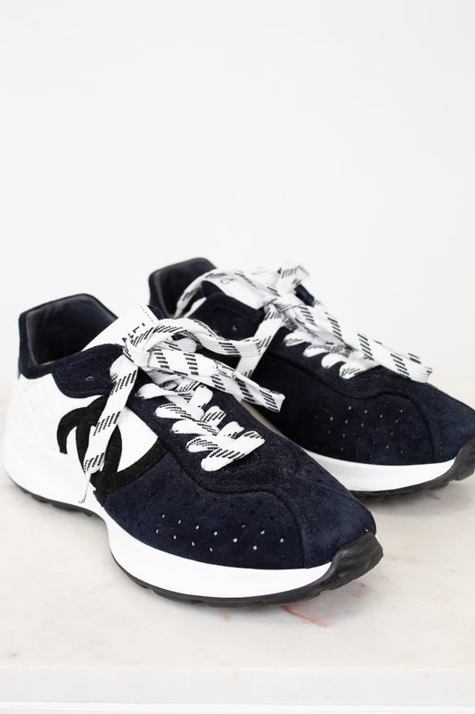 Pair of Chanel navy blue sneakers with white laces on a light gray background