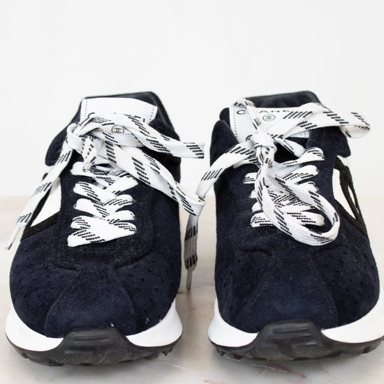 Pair of navy blue sneakers with white laces on a light gray background
