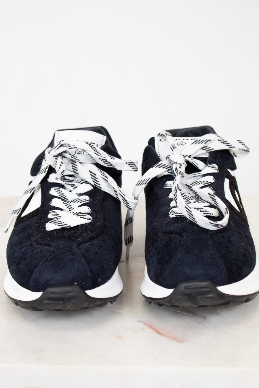 Pair of navy blue sneakers with white laces on a light gray background