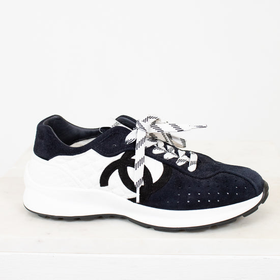 Pair of Chanel navy blue sneakers with white laces on a light gray background