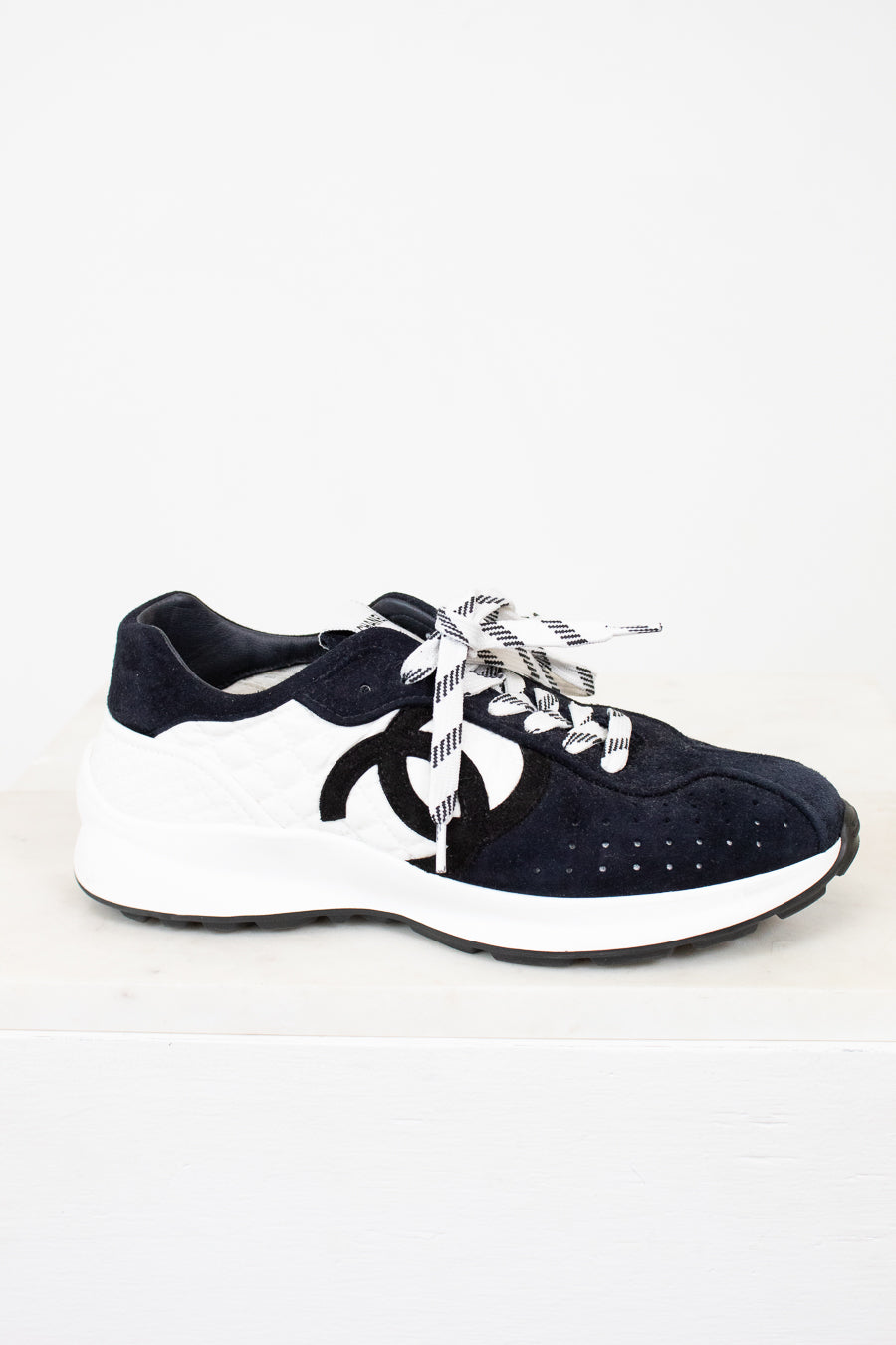 Pair of Chanel navy blue sneakers with white laces on a light gray background