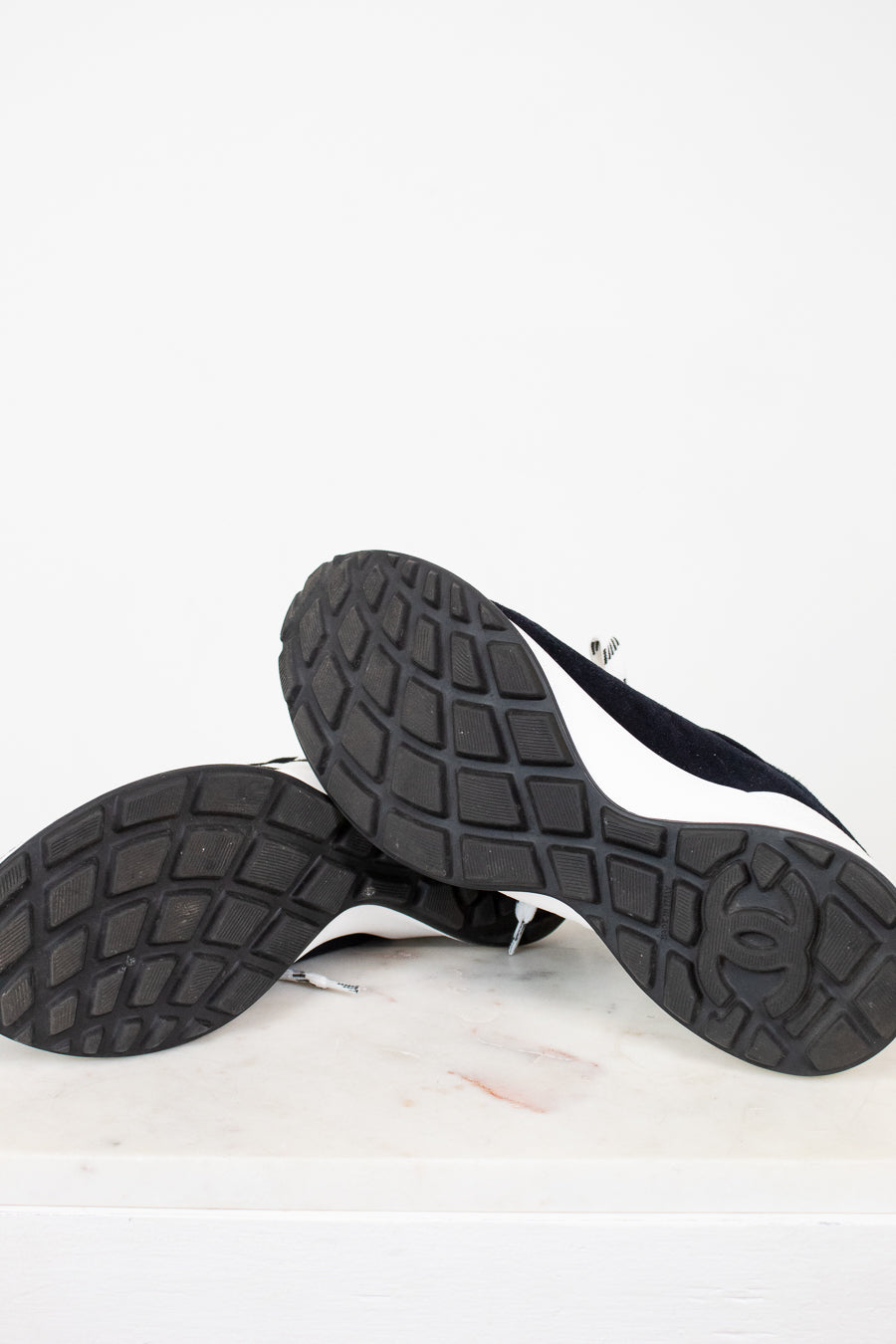 Pair of Chanel navy blue sneakers with white laces on a light gray background