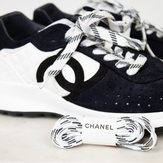 Pair of Chanel navy blue sneakers with white laces on a light gray background