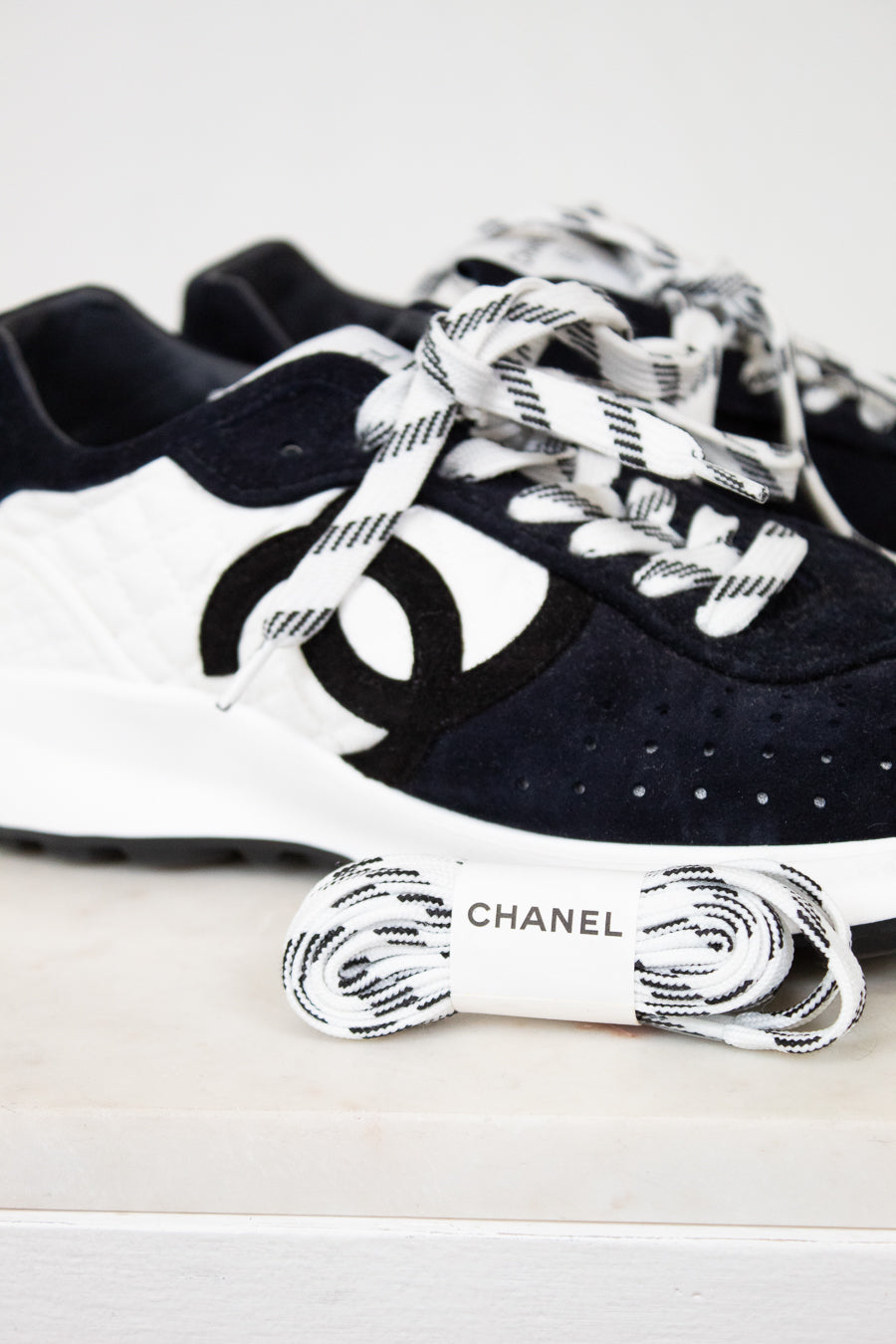 Pair of Chanel navy blue sneakers with white laces on a light gray background