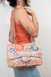 Person holding a floral quilted handbag with a visible brand logo against a plain background