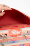 Close-up of a red interior of handbag with floral pattern inside, held by a hand.