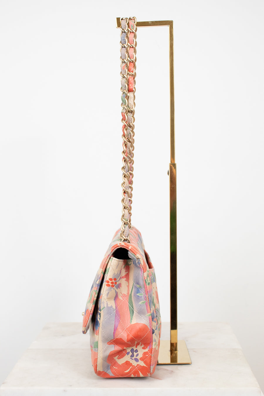 Side view of floral patterned handbag with a gold chain strap on a white background