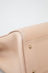 Close-up of a beige leather bag with gold hardware on a light gray background