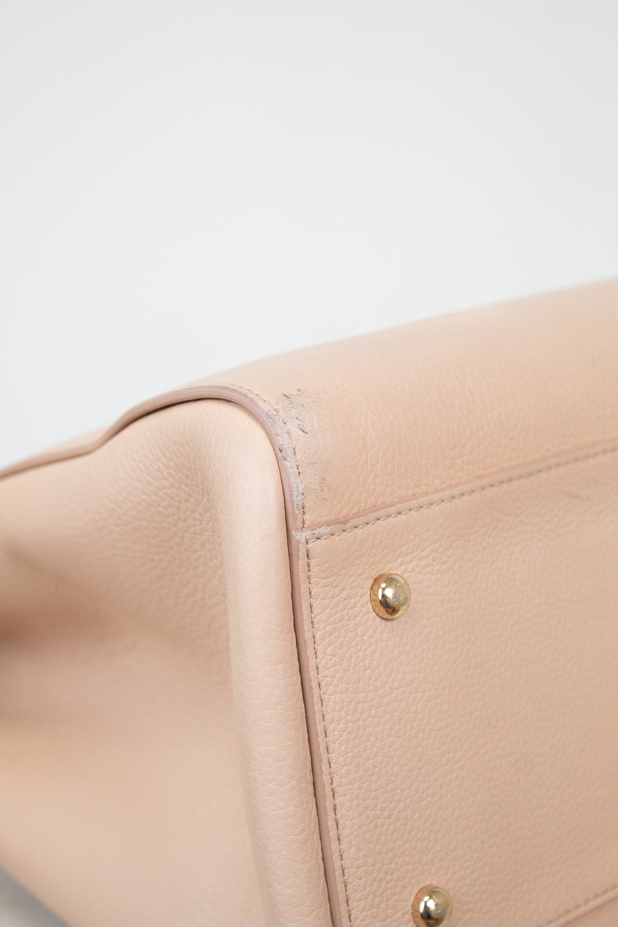 Close-up of a beige leather bag with gold hardware on a light gray background