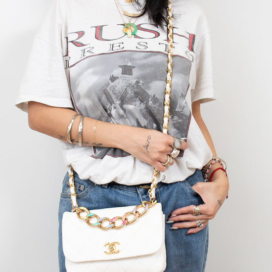 Person wearing a graphic t-shirt and jeans, holding a white handbag with gold chain strap.