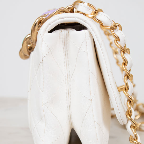 Side view of white quilted handbag with gold chain strap on a light gray background