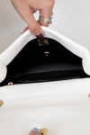 Close-up of a hand opening a white handbag with a black interior.