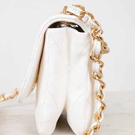 Side view of white quilted purse with gold chain strap on a light background