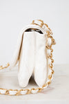 Side view of white quilted purse with gold chain strap on a light background